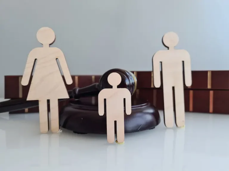 Wooden figures in front of a gavel represent parents and a child in a child custody case.