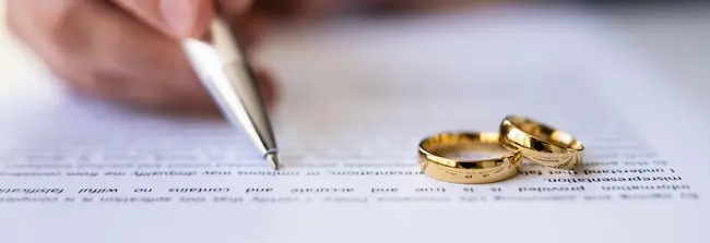 A person is signing divorce documents with wedding rings, symbolizing assets and support division during marriage dissolution proceedings.