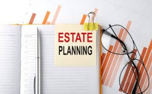A yellow notecard reading "ESTATE PLANNING" is clipped to a planner with a pen, glasses, and financial charts highlighting common estate planning mistakes to avoid.